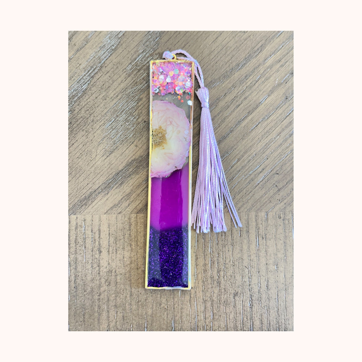 Example of a sold custom gold bezel bookmark with purple resin, glitter, flower, and tassel